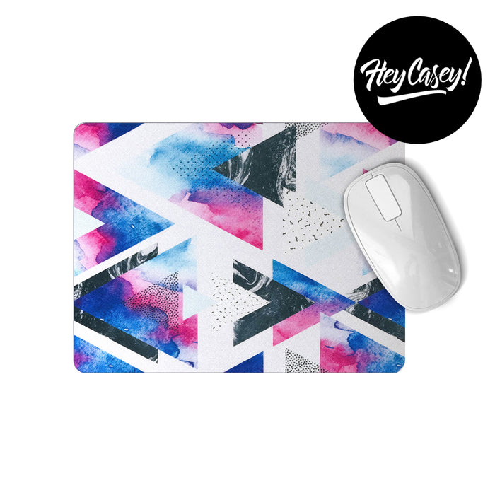 A white mousepad with a geometric design in blues, purples, pinks and black